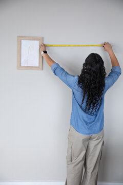 African american woman measuring gray wall at home using tape measure next to framed art print