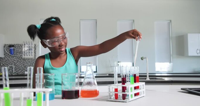African teen girl following tablet goggles-on drawing orange flask with pipette into rack at school