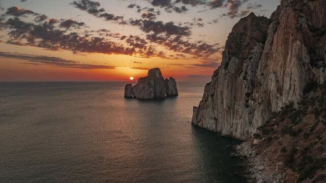 Sunset over Pan di Zucchero sea stack in Masua, Sardinia, Italy. Dramatic coastal landscape with golden sky and Mediterranean Sea at dusk