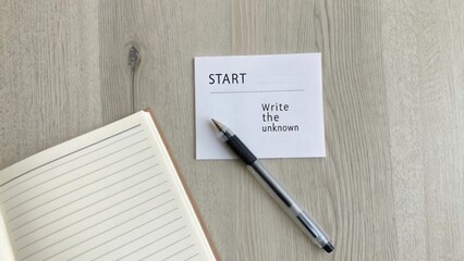 A minimal tabletop scene with a pen beside a 'Start Write the Unknown' note and an open notebook, ready for ideas.