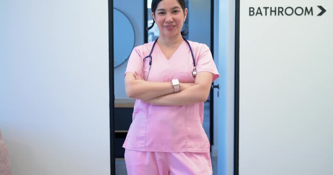 Woman in pink scrubs entering clinic walking up to camera stopping and showing stethoscope greeting