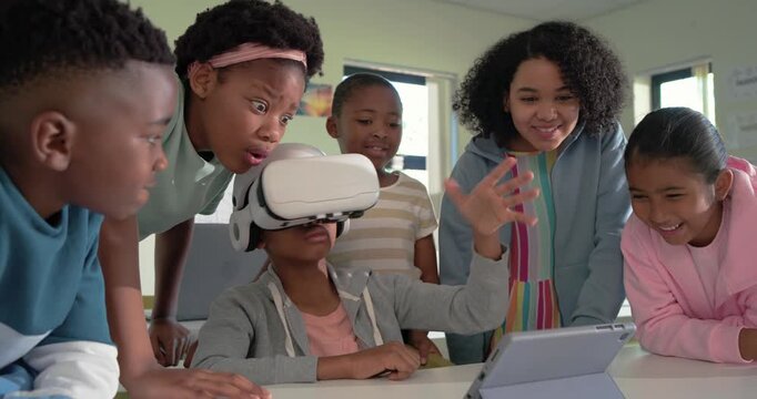 Diverse preteens watching African American girl donning white VR headset and using tablet for class