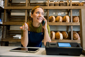 Smiling bakery owner taking order by mobile phone at counter