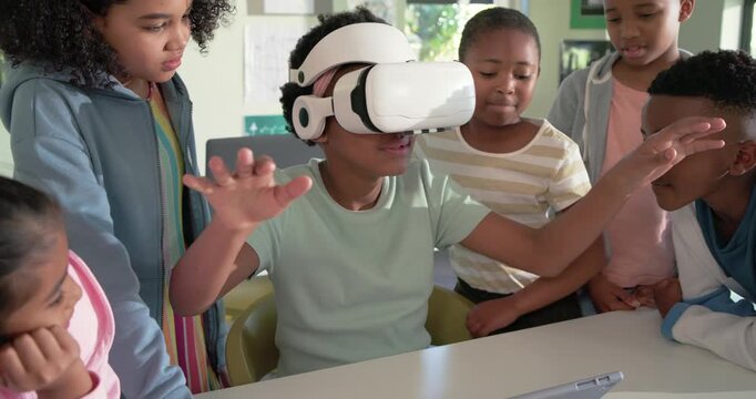 African-American teen girl with VR headset, mint tee, gesturing to VR demo, tapping tablet in class