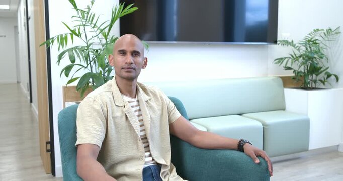 African American man shifting torso, following offscreen cue and smiling, sitting in teal armchair