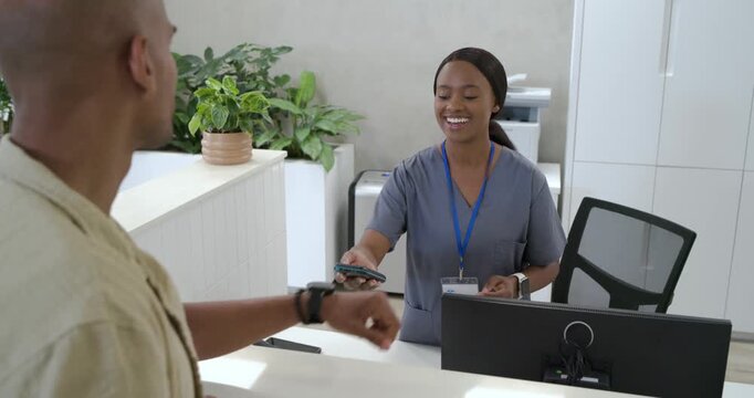 Scrub-clad woman clerk tapping phone scanning watch for checkin as man coming from left at desk