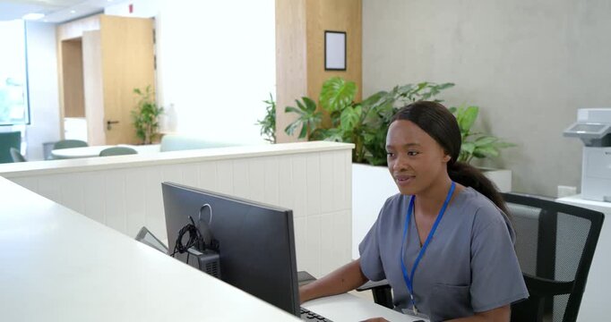 African woman at reception desk receiving checkin alert on monitor, typing and smiling, copy space