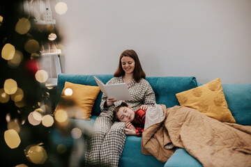 Mother reading bedtime story to child on couch near Christmas tree