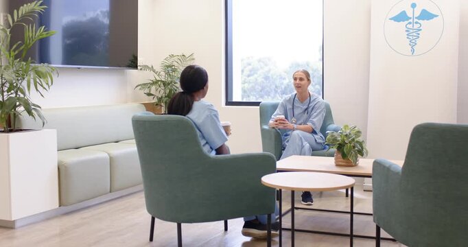 Diverse female coworkers in blue scrubs sharing coffee after grabbing cups, conversing in staffroom