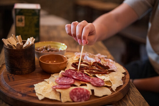 Close-up of a person picking cured meats with a toothpick from a traditional Italian charcuterie board served on a wooden table
