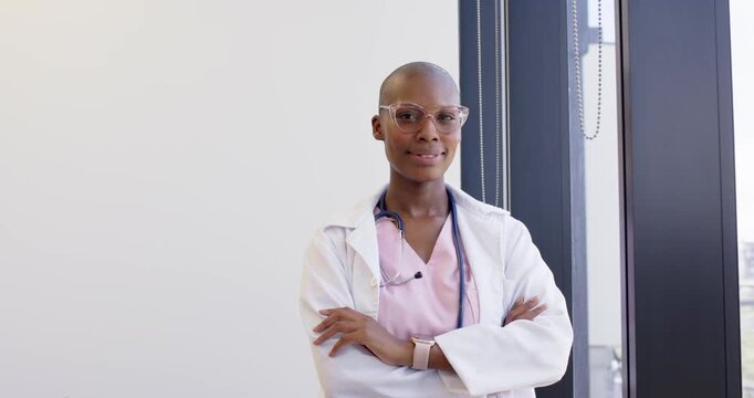 African woman medic by vertical window responding to camera, smiling, wearing lab coat, stethoscope
