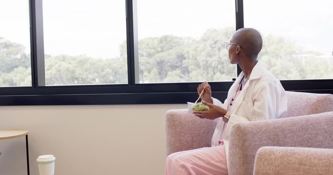Settling into pink armchair, hand is lifting fork, stirring salad near window during break