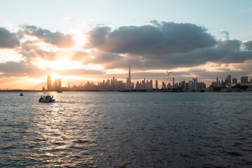 Obraz premium Dubai skyline at golden hour with dramatic sunset sky and calm water waves, Dubai Creek Harbor view 4k wallpaper background