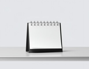 Black desk calendar with blank white pages, sits on a white surface
