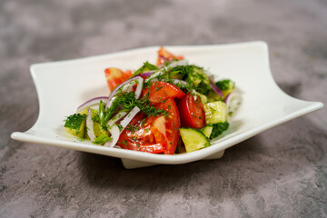 Fresh salad with diced tomatoes, cucumbers, and onions served on a white plate at a dining table