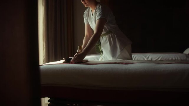 A spa therapist prepares a luxurious massage bed with essential oils, setting the scene for relaxation and wellness. The tranquil atmosphere invites a peaceful and rejuvenating experience.