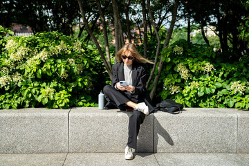 Successful businesswoman on break in park relaxing outside of office building, enjoying sunny...