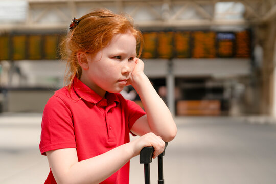 Young girl waits at train station with suitcase during travel delay