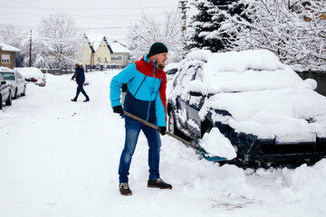 Man removes snow near car on a winter morning, outside his home in a residential area