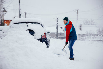 Man removes snow near car on a winter morning, outside his home in a residential area