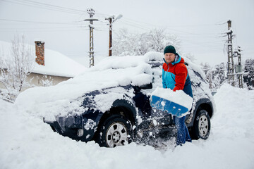 Man removes snow near car on a winter morning, outside his home in a residential area