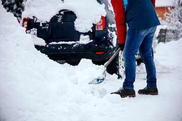 Man removes snow near car on a winter morning, outside his home in a residential area