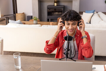 Naklejka premium Man speaking into microphone wearing headphones, using laptop at table in living room