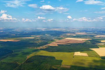 Aerial view of vast green plains and small villages taken from airplane window during summer flight