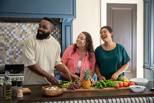 Diverse friends chopping vegetables using knife on wooden kitchen island with fresh produce - Powered by Adobe