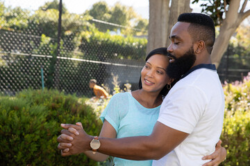 Diverse couple dancing holding hands in garden under trees near chain-link fence wearing wristwatch © wavebreak3