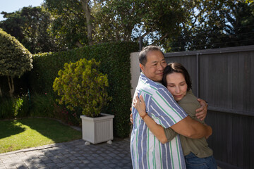Diverse couple hugging on stone paver patio with trimmed shrub and fence in sunlight