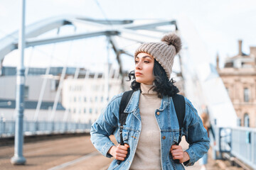 Woman on bridge wearing hat and backpack during daytime in urban area