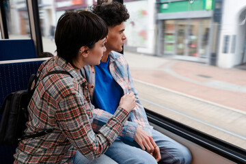 Friends sit close on public transport while looking outside the window at passing scenery