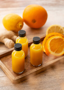 Three glass bottles of orange ginger immunity shots with fresh citrus fruits on a wooden tray.