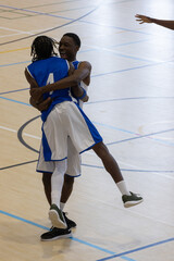 Basketball players in blue uniforms celebrating after scoring on polished wooden court