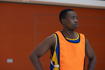 African american man looking right in gym court wearing orange bib over jersey by padded wall