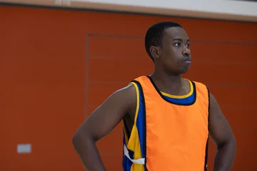 Fotobehang Onderzeeër African american man looking right in gym court wearing orange bib over jersey by padded wall  © wavebreak3
