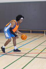 Naklejka premium African american male basketball player dribbling basketball on gym court, copy space