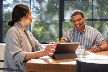 Diverse colleagues in business attire pointing at tablet, notepad at office table, copy space