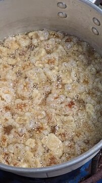 ​Freshly fried crispy pork rinds in a slotted spoon over a pot of oil. Traditional Thai snack "Kab Moo" process.