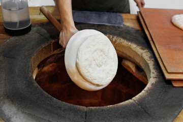 Baker putting fresh dough into a hot tandoor oven for baking. Traditional bread making process.