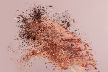 A scattered dry mixture of textures in different shades of brown eyeshadow on a beige background. The concept decorative cosmetics. view. copy space.