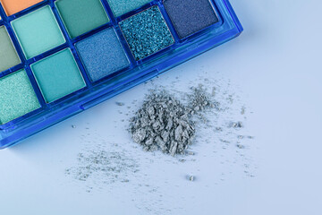 Blue pack of palete with blue shades of eye shadow with glitter, shimmer on a light blue background with a pile of scattered eyeshadows. top view.