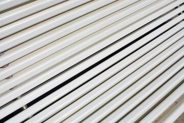 A close up shot of white plastic bench slats creates a repetitive linear pattern with diagonal perspective and soft shadows.