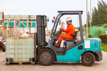 Industrial Worker in Protective Gear Operating a Forklift to Transport Large Liquid Containers in a Manufacturing Facility © agung