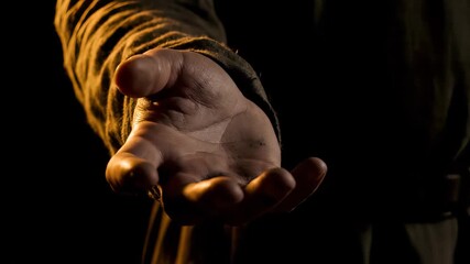 Distressed person's rough hand held out, palm open, dramatically lit against a dark background, concept for poverty awareness, humanitarian aid and emotional struggle