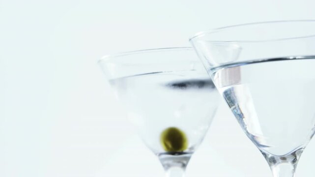 Video of olives falling into glasses of martini on white background