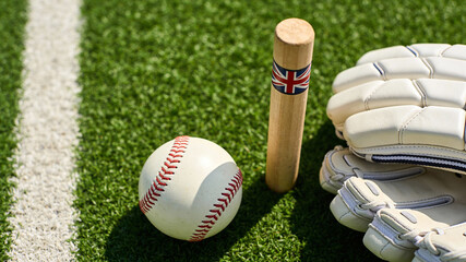 Baseball equipment and ball on green grass with a wooden wicket during a sunny day