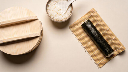 Flatlay of sushi preparation with rice and bamboo mat on a light surface