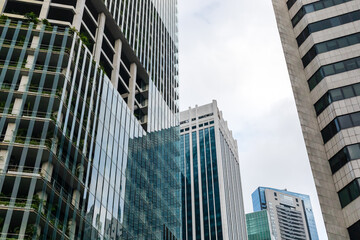 Obraz premium Tall buildings fill the city skyline. They have glass windows and concrete surfaces. The scene shows a mix of modern architecture under a cloudy sky